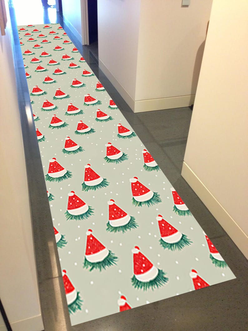 Op de afbeelding: Een lange, rechthoekige vloerkleed met een herhalend patroon van rode kerstmutsen op een lichtgrijze achtergrond. De mutsen hebben witte randen en zijn omgeven door groen, met kleine witte stippen verspreid.
