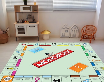 May include: A green and red Monopoly game board rug with the word "MONOPOLY" in red letters. The rug is on a white floor in a room with a play kitchen and a chair.