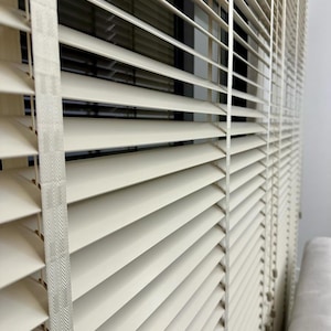 May include: White wooden blinds with a white tape edge. The blinds are closed and the slats are horizontal.
