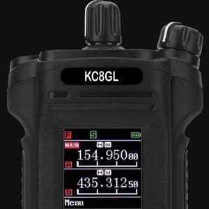 Puede incluir: Una radio de mano negra con una pantalla digital que muestra los números 154.9500 y 435.3125. La radio tiene una etiqueta que dice "KC8GL".