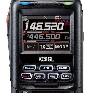 May include: A black handheld two-way radio featuring a digital display showing frequencies 146.520 and 446.500, the text KC8GL, and various control buttons labeled F MENU, A/B, BAND, GM/X, V/M, PMG, and BACK, with a top antenna and volume knob.
