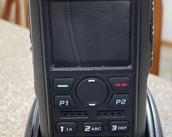 May include: A black two-way radio with a charging base. The radio has a screen, buttons, and the call sign "KC8GL" printed on the front. The charging base also has the call sign "KC8GL" printed on it.