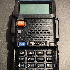 Puede incluir: Una radio bidireccional portátil de color negro con pantalla digital, antena y teclado numérico. El dispositivo incluye un botón naranja VFO/MR, un botón azul A/B y el texto WRFR362 y UV-5X impreso en la parte frontal de la carcasa.