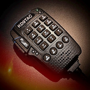 Puede incluir: Una radio de mano negra con un teclado y una pantalla de visualización. La radio tiene un teclado con letras y números, y una pantalla de visualización que muestra el texto "KD9TAC".