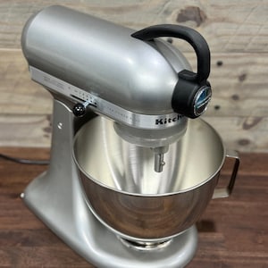 Könnte beinhalten: Silberfarbener KitchenAid Ultra Power Plus Küchenmixer mit einer Edelstahlschüssel und schwarzem Griff. Der Mixer hat einen Drehregler zur Geschwindigkeitsregelung und das KitchenAid-Logo ist sichtbar. Der Mixer steht auf einer Holzoberfläche.