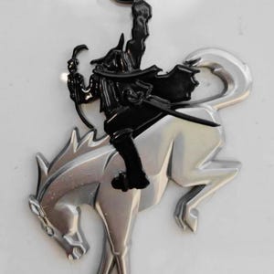 以下が含まれることがあります： カボチャを持った馬に乗ったライダーを描いた、シルバーとブラックのエンブレム。ライダーは黒い服を着ており、馬はシルバーです。「BIG BEND」の文字がエンブレムの下部にあります。