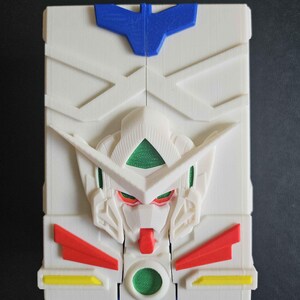 May include: A rectangular white plastic case featuring a moulded relief of a robot head in the centre. The design includes a blue crest at the top, green accents on the eyes and chest, red chin and side details, and small yellow rectangular accents.