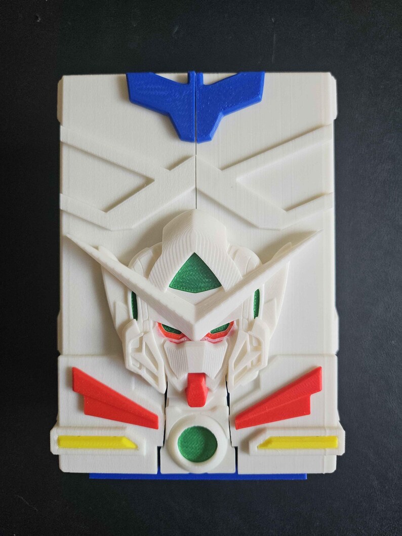 May include: A rectangular white plastic case featuring a moulded relief of a robot head in the centre. The design includes a blue crest at the top, green accents on the eyes and chest, red chin and side details, and small yellow rectangular accents.