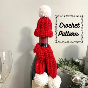 Pode incluir: Capa de garrafa de vinho de crochê vermelha com um chapéu e uma echarpe de pompom branco. Padrão de crochê.