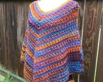 Puede incluir: Un poncho de ganchillo con cuello en V y un patrón a rayas en tonos de morado, azul, naranja y marrón.