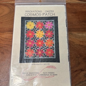 May include: A quilting pattern for a quilt called "Cosmos Patch" by Ruth Powers. The pattern features a black background with red, yellow, and orange flower-like shapes. The pattern is approximately 59 inches by 74 inches.