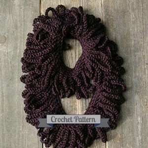 May include: A crocheted cowl in a deep purple color. The cowl is made with a series of loops and has a fringe-like texture. The cowl is photographed on a wooden surface. "Crochet Pattern" is written on a ribbon below the cowl.