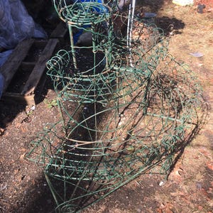 Könnte beinhalten: Ein dreistufiger Pflanzenständer aus Metall mit grüner Oberfläche. Jede Stufe ist herzförmig und hat ein Drahtgitterdesign. Der Ständer ist aus robustem Metall gefertigt und eignet sich perfekt zum Präsentieren von Pflanzen oder Blumen.