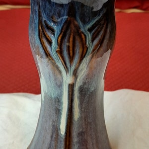 May include: A handcrafted ceramic vase with a flared top and a unique, organic design. The vase features a blend of blue, brown, and white glaze, creating a visually appealing aesthetic. The vase is approximately 10 inches tall.