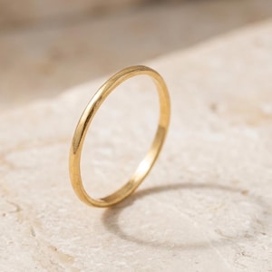 Peut inclure: Une fine bague anneau en or poli avec une surface lisse et arrondie. La bague présente un design circulaire simple et continu avec une finition métallique réfléchissante, affichant une apparence propre et uniforme sur toute la circonférence.