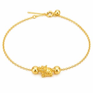 Può includere: Un bracciale a catena color oro con un ciondolo centrale a forma di creatura mitica drago-tartaruga. Il ciondolo è affiancato da due sfere dorate lucide su entrambi i lati. Il bracciale è fissato con una chiusura a molla circolare e una perlina.