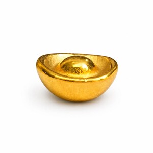 May include: A gold-colored ingot, a traditional symbol of wealth and prosperity. The ingot has a rounded shape with a raised central portion, and a smooth, reflective surface. The background is plain white.
