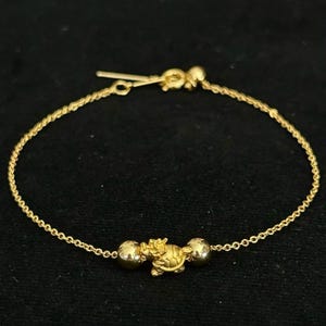 May include: A delicate gold chain bracelet featuring a central charm shaped like a small turtle, flanked by two smooth, polished gold spherical beads. The bracelet is secured with a gold spring ring clasp and a short extender chain at the end.