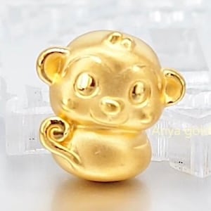 May include: A gold-colored monkey charm with a rounded body, large eyes, and prominent ears. The charm has a smooth, polished finish and a curled tail. The charm is likely a pendant or bead.