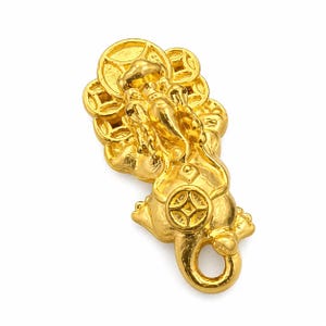 May include: A gold-colored figurine of a mythical creature, possibly a dragon or lion, with coin-like details. The figurine has a loop at the tail end, suggesting it could be a pendant or charm. The design is intricate and detailed.