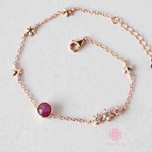 May include: A delicate rose gold bracelet featuring star charms and a central round, pink gemstone. Additional small clear gemstones and a lobster clasp complete the design. The bracelet is a stylish piece of jewellery.