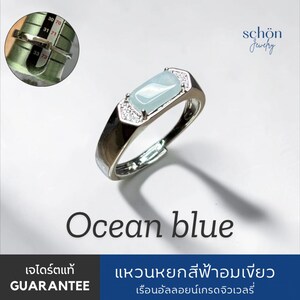 Peut inclure: Une bague argentée avec une pierre rectangulaire bleu-vert pâle au centre, entourée de petites pierres claires. Un encart circulaire montre la bague sur un triboulet, indiquant une taille entre 71 et 73. Le texte indique Ocean blue.