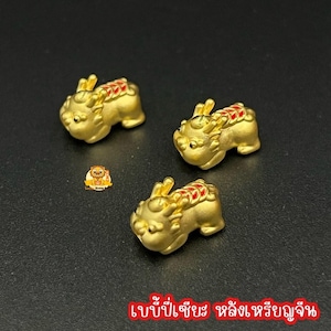 May include: Three gold-colored, miniature mythical creature figurines with red and gold accents. The figurines are in a crouching position, with detailed features. The background is a dark, solid color. Text in Thai is at the bottom.