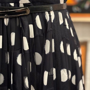 May include: A black and white polka dot dress with a black belt. The dress is pleated and has a loose fit.