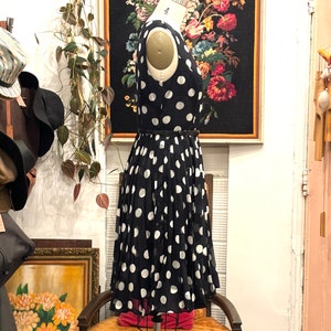May include: A black and white polka dot dress with a black belt. The dress is on a mannequin and is in a store setting.