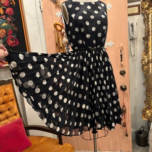 May include: A black and white polka dot dress with a fitted bodice and a full skirt. The dress has a black belt and is sleeveless.