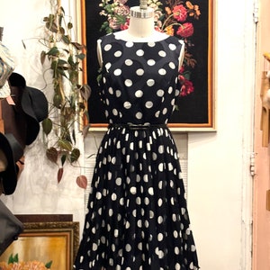 May include: A black and white polka dot dress with a pleated skirt. The dress is sleeveless and has a black belt.