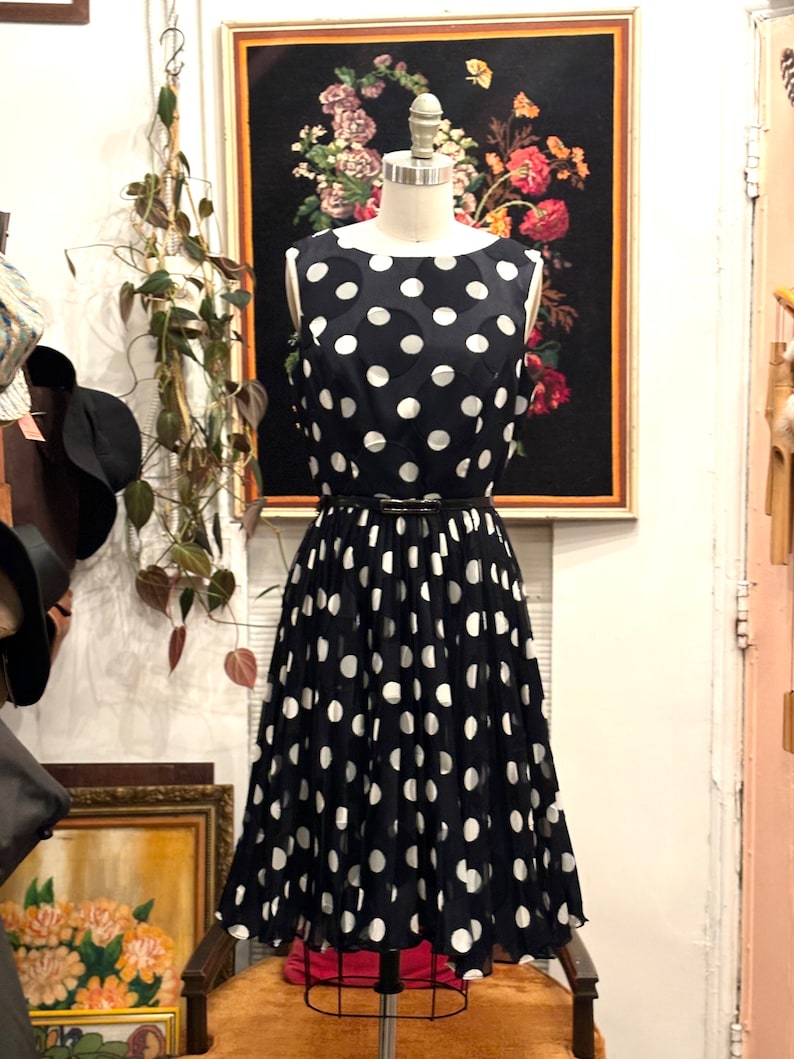May include: A black and white polka dot dress with a pleated skirt. The dress is sleeveless and has a black belt.