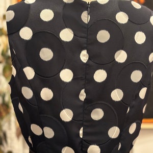 May include: A black sleeveless dress with a white polka dot pattern. The dress has a black belt and a zipper in the back.