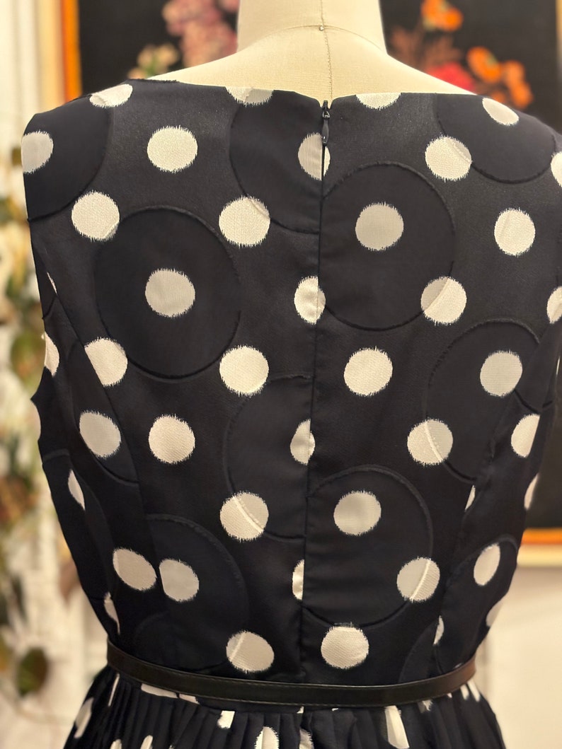 May include: A black sleeveless dress with a white polka dot pattern. The dress has a black belt and a zipper in the back.