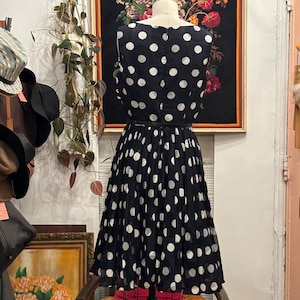 May include: A black and white polka dot dress with a fitted bodice and a full skirt. The dress is sleeveless and has a round neckline.