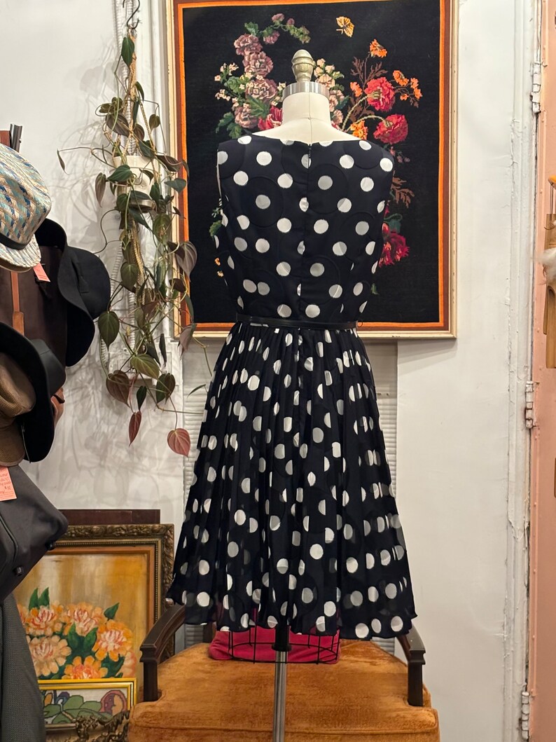 May include: A black and white polka dot dress with a fitted bodice and a full skirt. The dress is sleeveless and has a round neckline.