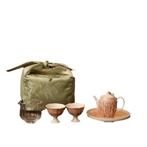 May include: A complete tea set featuring a light green satin bag with a bamboo leaf pattern, a clear glass pitcher, two small teacups, a teapot, and a serving tray. The teapot and teacups have a reddish-brown floral design.