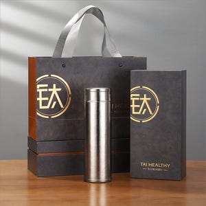 May include: A stainless steel insulated tumbler, gift box, and shopping bag set. The dark grey packaging has gold accents and Chinese characters. The text "TAI HEALTHY" is printed on the box. The tumbler is approximately 20 cm tall.