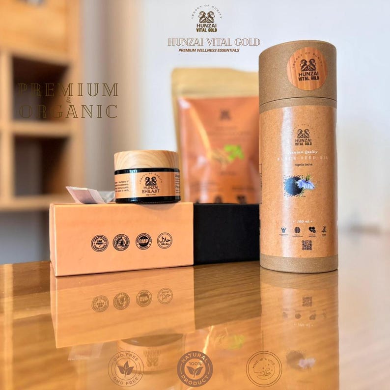 以下が含まれることがあります： Hunzai Vital Goldのウェルネス製品の詰め合わせ。画像には、シラジットの瓶、箱、ポーチ、黒種子油の円筒容器が写っています。「Premium Organic」の文字が見える反射面に製品が展示されています。
