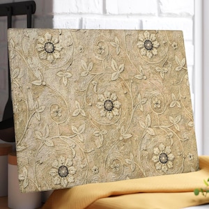 May include: A rectangular decorative panel with a raised floral and leaf design. The panel features a beige background with embossed flowers and swirling vines. The flowers have dark centers, and the leaves are detailed with veining.