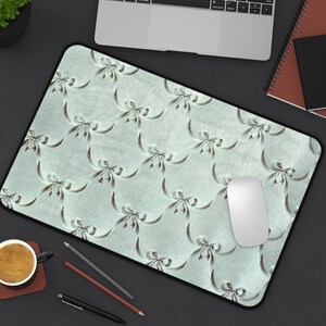 以下が含まれることがあります： 薄い青色のマウスパッドに、茶色のリボンが繰り返し模様として描かれています。白いコンピューターマウスがパッドの上に置かれています。