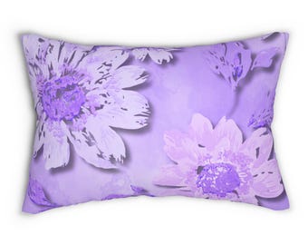 May include: Rectangular decorative pillow with a floral pattern. The pillow features large, stylized flowers in shades of purple and lavender against a light purple background. The flowers have detailed petals and dark purple centers.