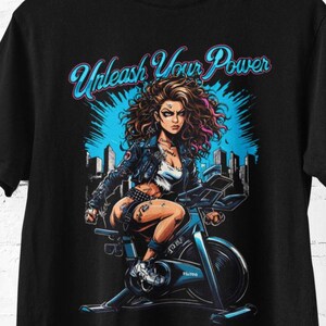 Könnte beinhalten: Schwarzes T-Shirt mit einer Grafik einer Frau auf einem Heimtrainer. Der Text "Unleash Your Power" ist in Blau und Pink gehalten. Die Frau hat pinkfarbene Haarsträhnen und trägt ein weißes Oberteil und eine schwarze Jacke.