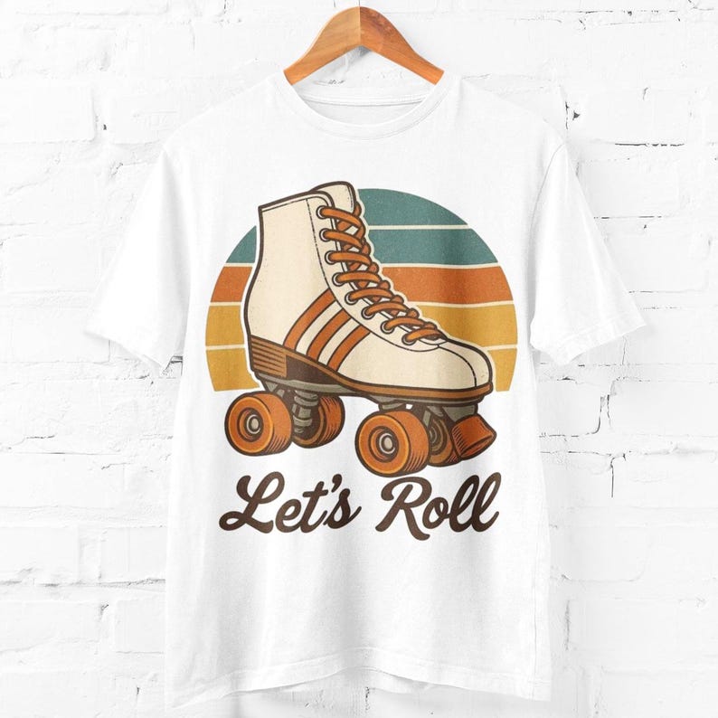 May include: White t-shirt with a vintage roller skate design in cream and orange, set against a sunset backdrop. The words "Let's Roll" are printed below the graphic. The t-shirt is displayed on a wooden hanger.