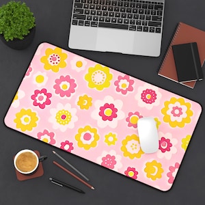 May include: A pink rectangular mousepad with a floral pattern in yellow, pink, and white. The mousepad is on a dark surface, with a laptop, mouse, and other office supplies visible.