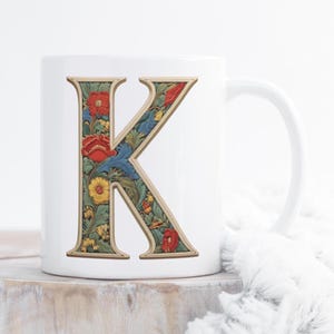 Può includere: Tazza in ceramica bianca con una lettera K floreale con bordo dorato. La lettera è piena di un motivo floreale colorato.