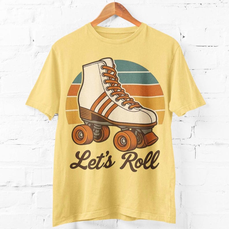 May include: Yellow t-shirt with a retro roller skate design. The graphic shows a white and orange roller skate against a sunset backdrop, with the words "Let's Roll" in a cursive font. The shirt is displayed on a wooden hanger.