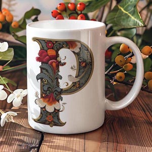 May include: White ceramic mug with a floral design featuring the letter "P" in a decorative font. The mug has a handle and is sitting on a wooden surface.