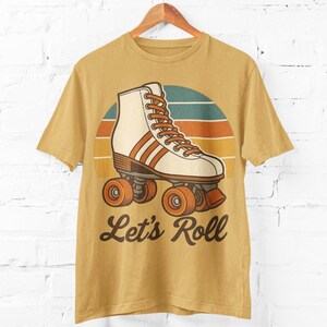 May include: Mustard yellow t-shirt with a retro roller skate design. The graphic features a white and brown roller skate with orange wheels and laces, set against a sunset background. The text "Let's Roll" is below the skate.