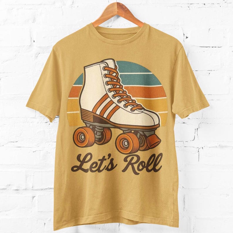 May include: Mustard yellow t-shirt with a retro roller skate design. The graphic features a white and brown roller skate with orange wheels and laces, set against a sunset background. The text "Let's Roll" is below the skate.